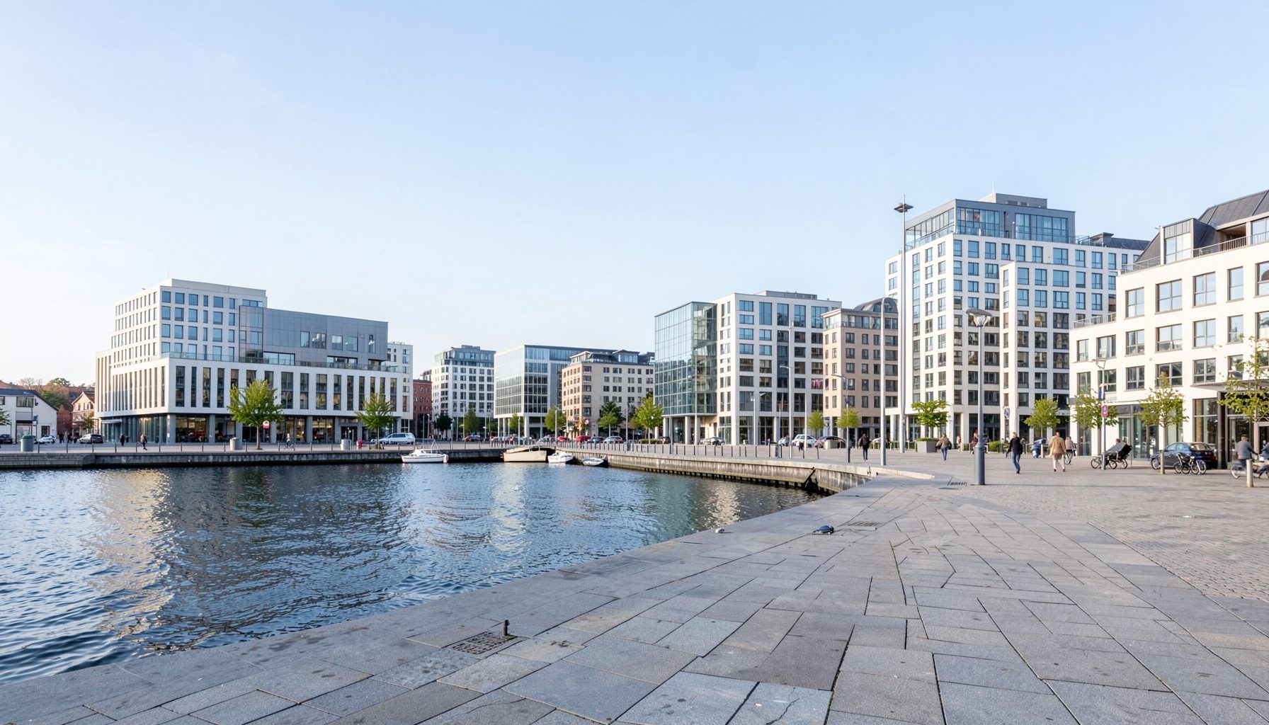 A modern Scandinavian cityscape with clean architecture, waterfront promenade, and a pale blue sky.